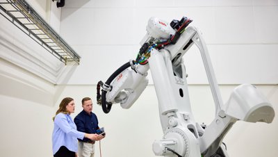 Két mérnök programoz egy nagy, fehér ABB ipari robotkart egy laboratóriumi környezetben.