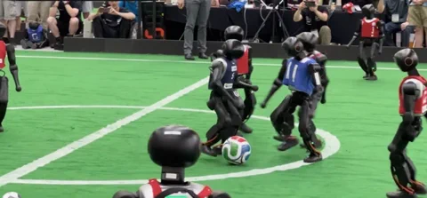 Két humanoid robotcsapat futballozik a zöld gyepen a RoboCup 2026 első 11 a 11 elleni mérkőzésén.